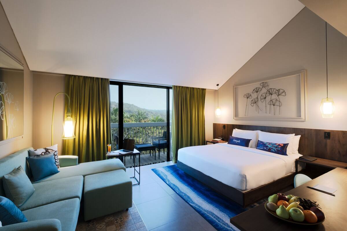 Quarto de hotel com cama grande, sofá, mesa de jantar e varanda com vista.