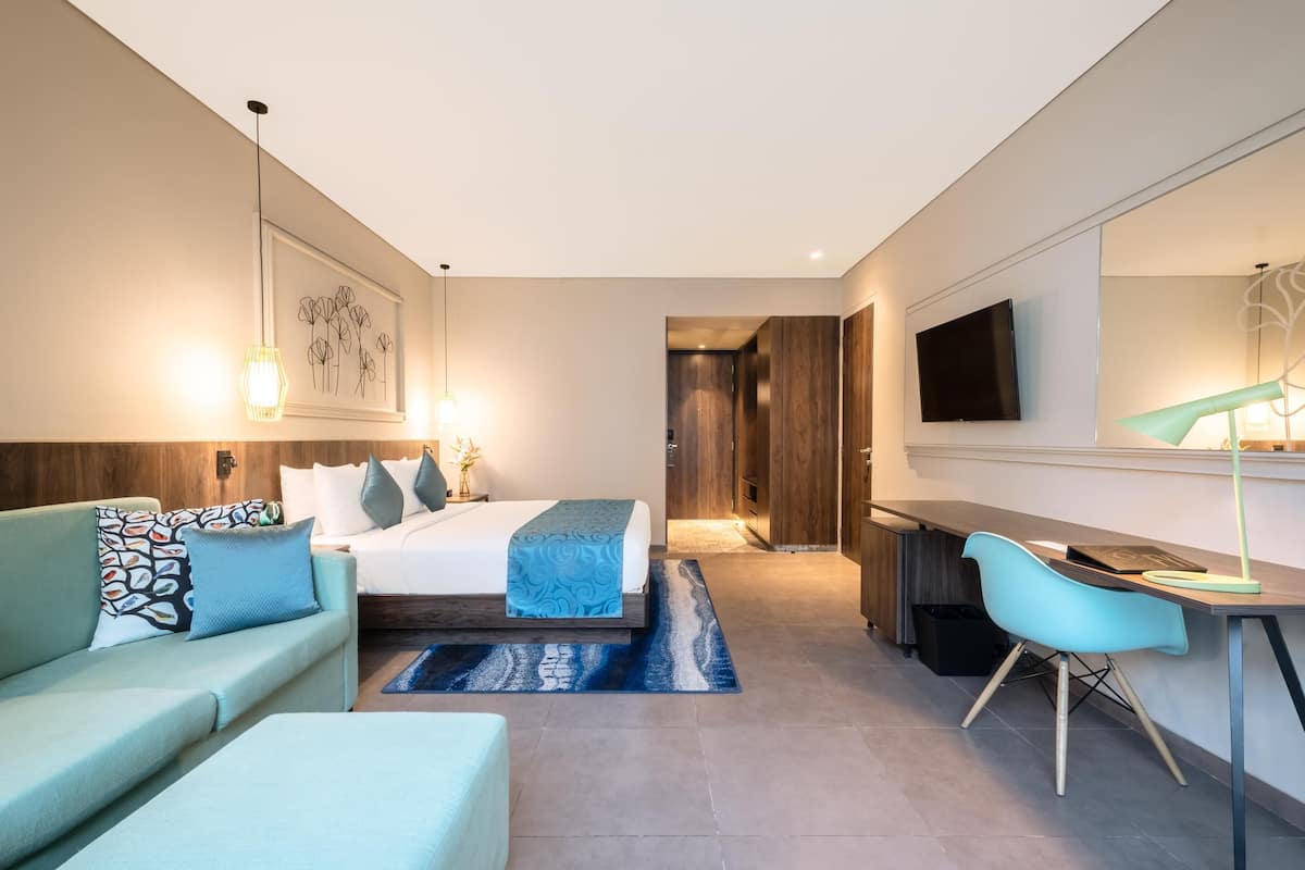 Quarto de hotel moderno com cama, escrivaninha, cadeira, sofá e televisão.