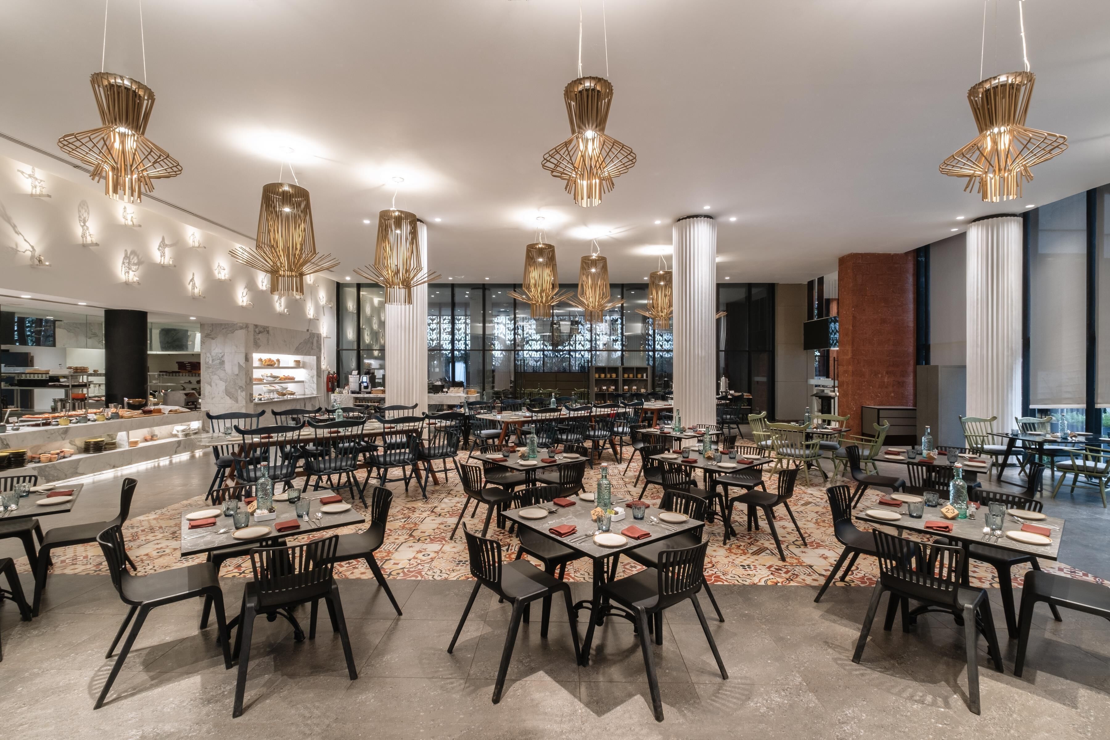 A spacious dining area with multiple tables and chairs, modern pendant lighting, and a view of the kitchen in the background.