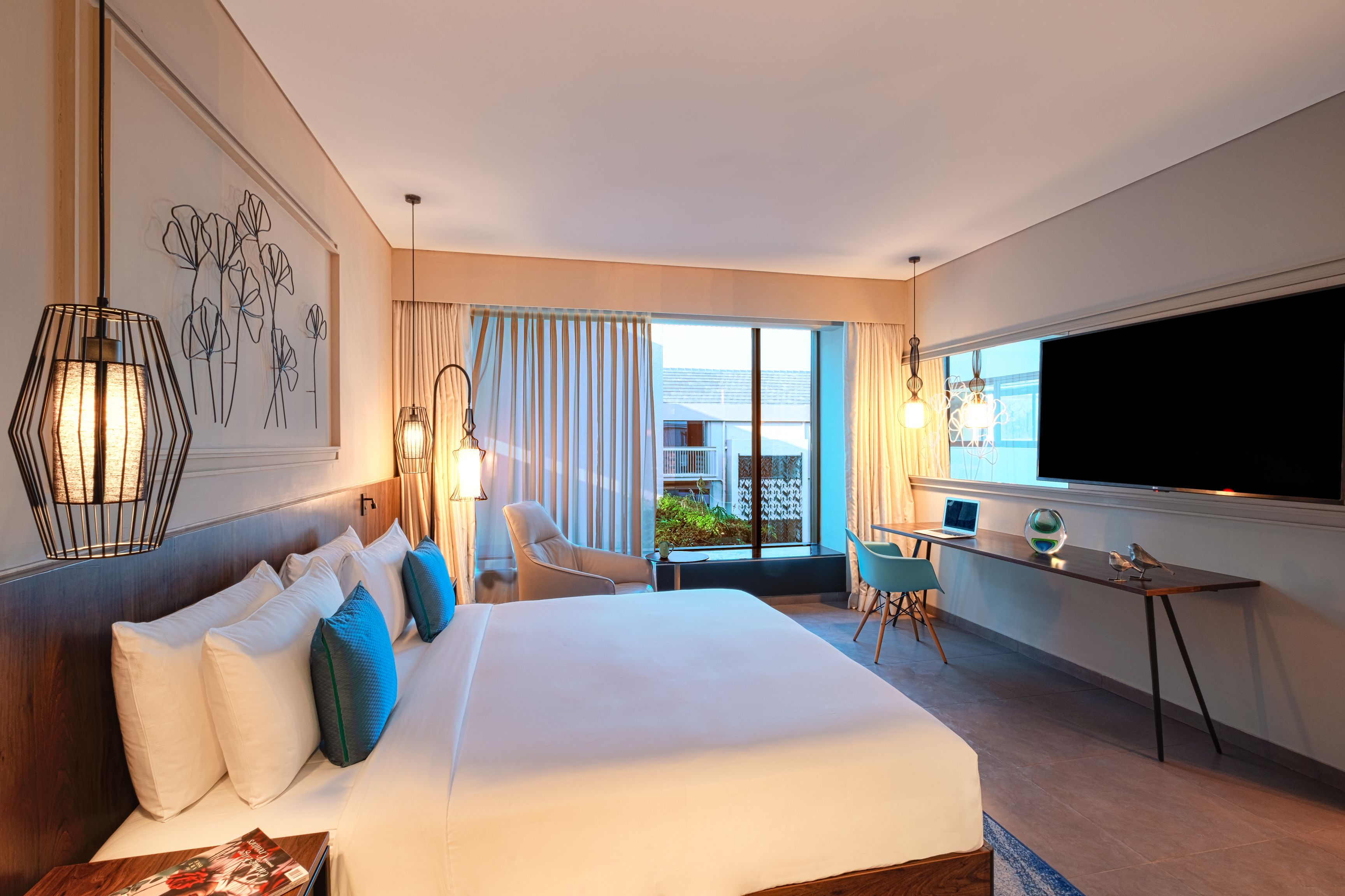 A hotel room with a large bed, a desk with a laptop, a TV, and a view of the outdoors.