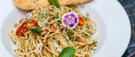 A plate of spaghetti with a basil leaf garnish, a small purple flower, and a piece of bread on a white plate.