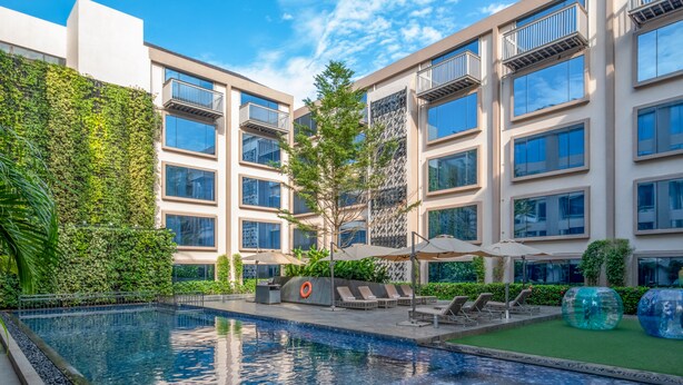 A modern building with a swimming pool, outdoor seating, and a green wall.