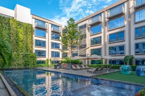 Un edificio moderno con piscina, asientos exteriores y una pared verde.