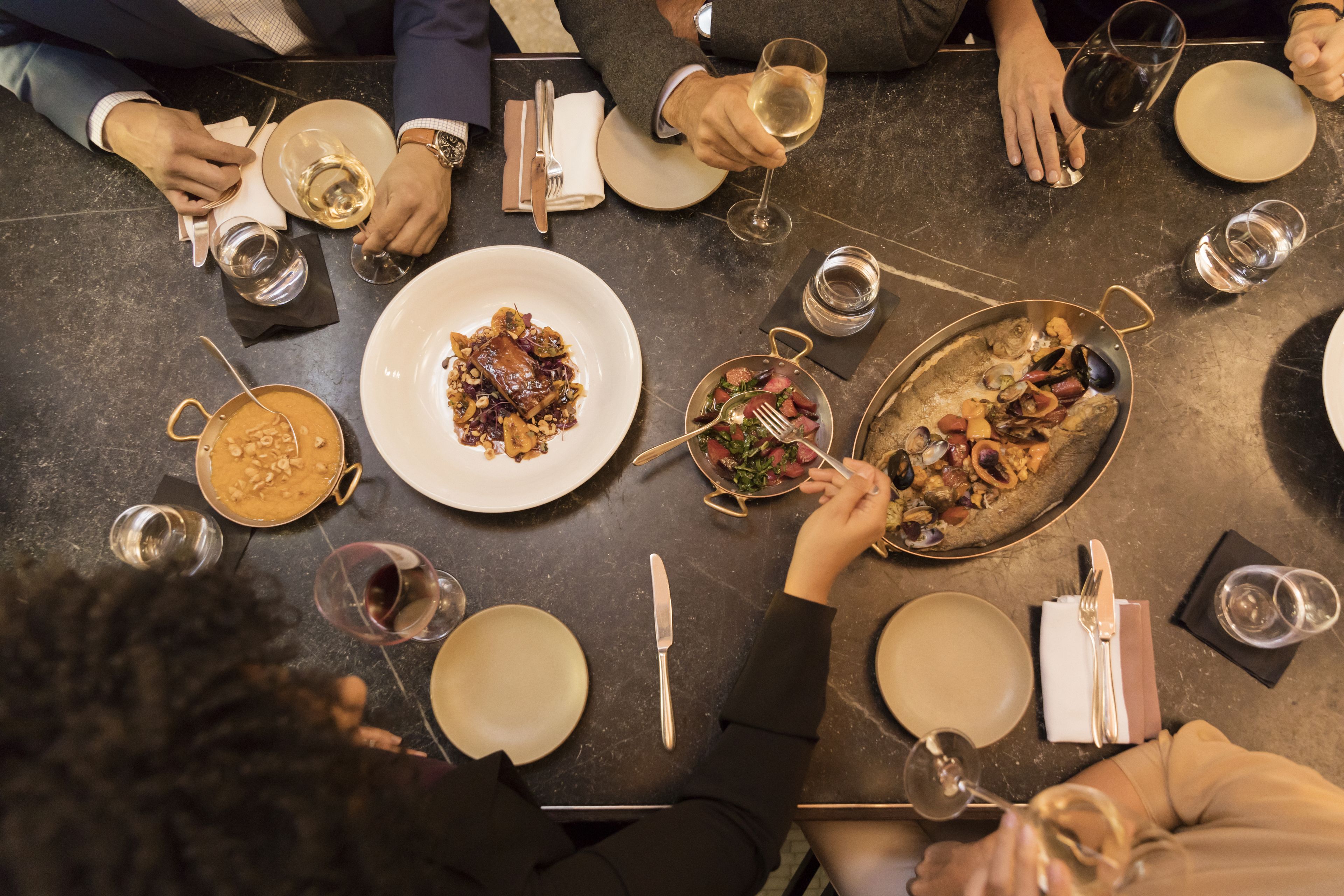 Un groupe de personnes est réuni autour d’une table, où l’on peut voir différents plats et des verres de vin.
