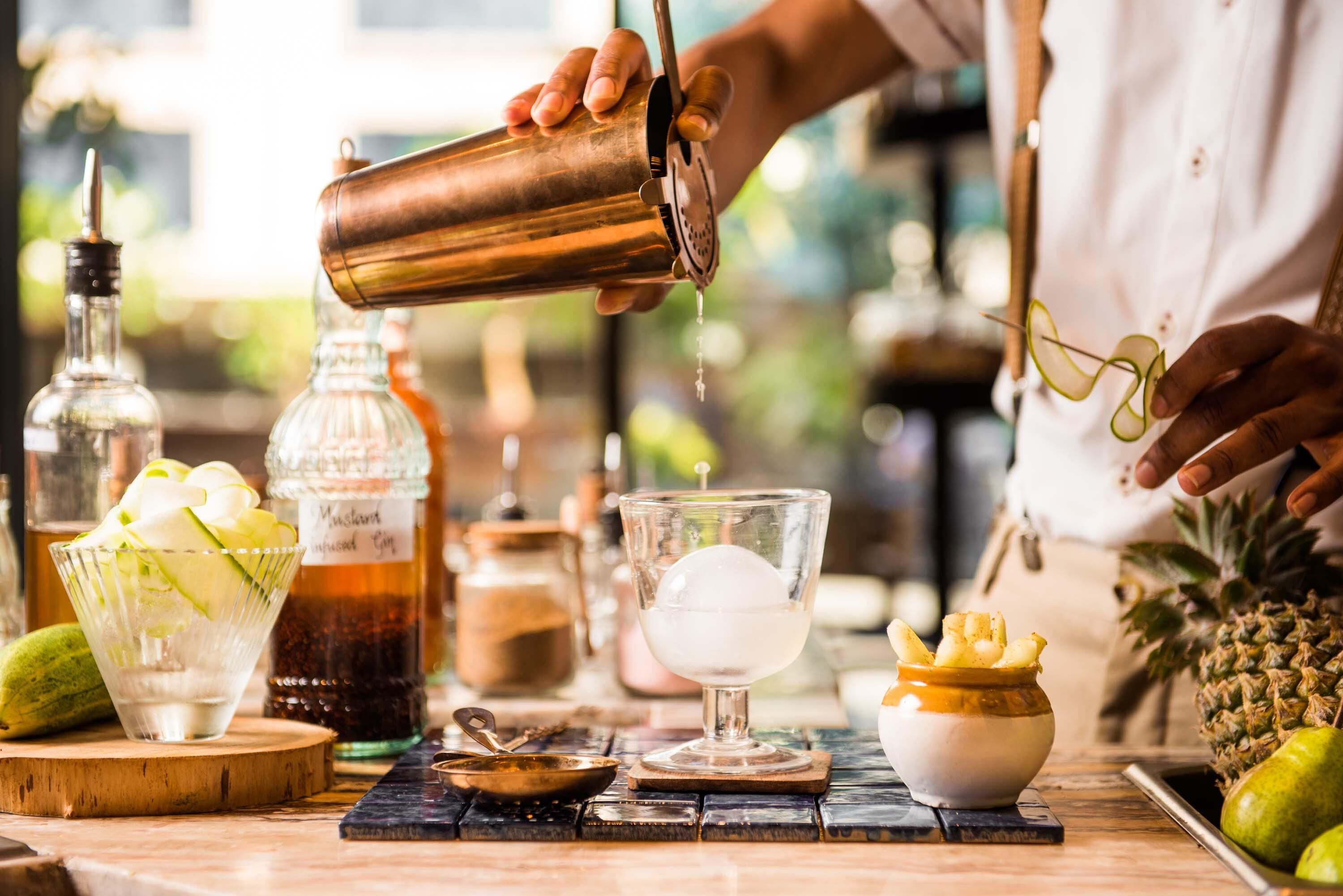 Un bartender sirviendo una bebida en un vaso, con varias botellas y una piña en la barra.