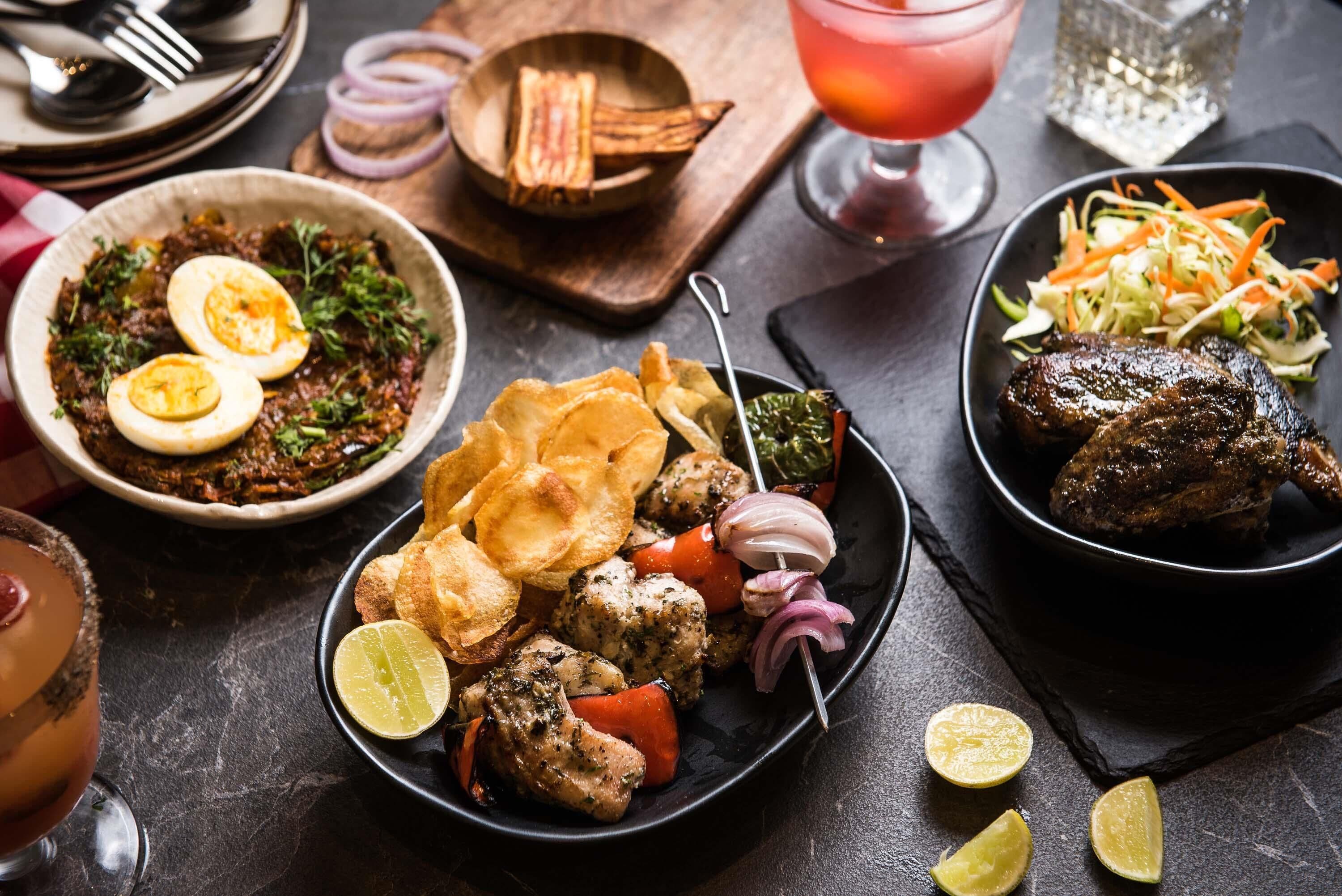 A variety of dishes including grilled meat, vegetables, and a salad, along with a drink and bread.