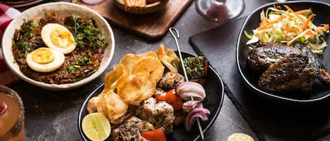 A variety of dishes including grilled meat, vegetables, and a salad, along with a drink and bread.