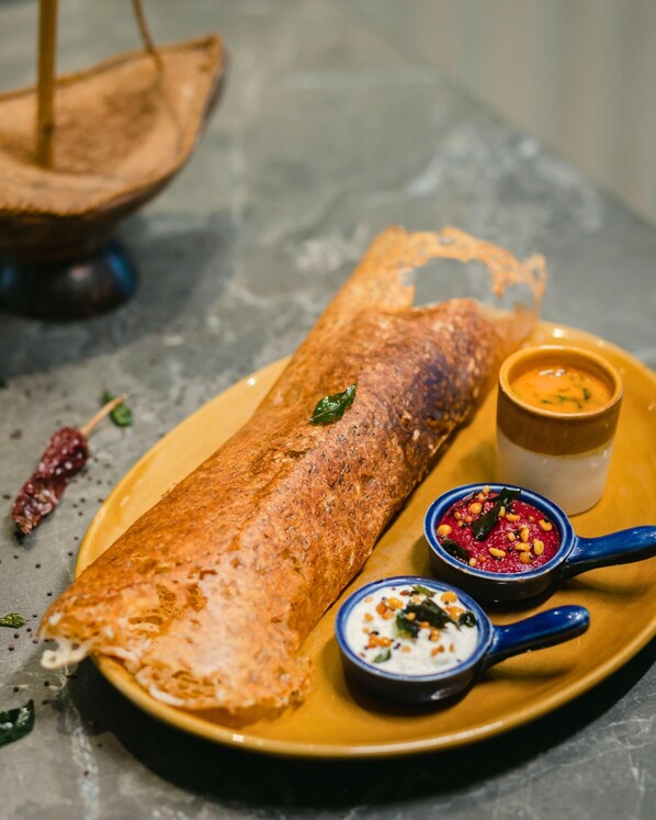 Un plato con una crepe enrollada, dos recipientes pequeños con salsas y una cuchara de madera.