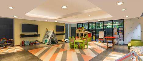 Amplia sala de juegos infantiles con un gran ventanal, una casita de juegos y diversos juguetes y materiales educativos.