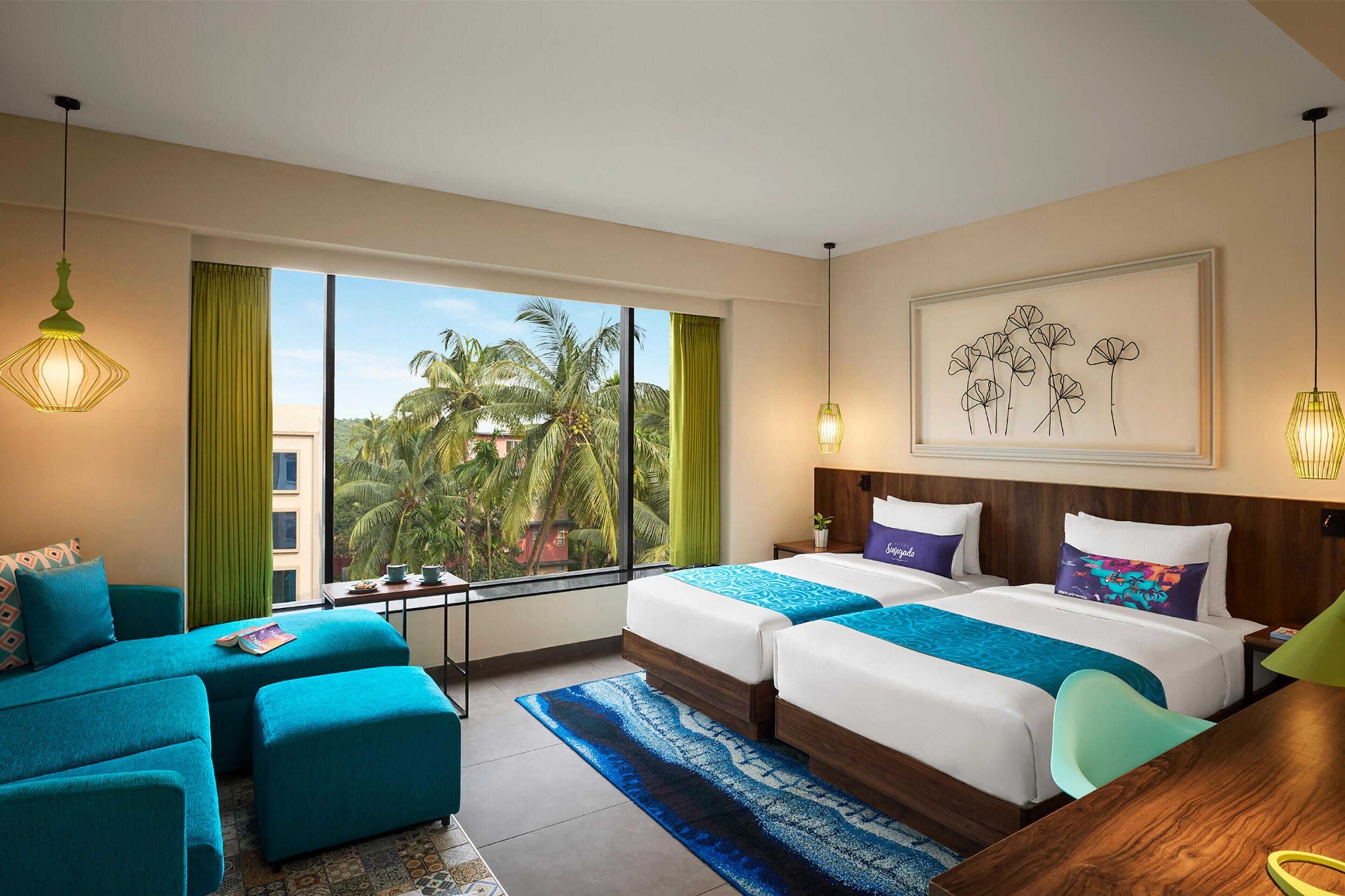 Habitación de hotel con dos camas, un sofá y vista a palmeras.