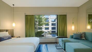 Una habitación de hotel con cama, sofá, una mesita y ventana con cortinas.