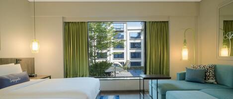A hotel room with a bed, a sofa, a small table, and a window with curtains.