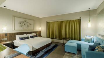 A hotel room with a large bed, a desk with a chair, a sofa, and a window with curtains.