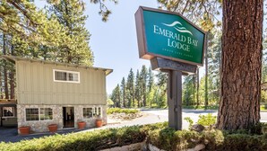 Un alojamiento llamado 'Emerald Bay Lodge' con fachada de piedra, un letrero y un estacionamiento rodeado de árboles.
