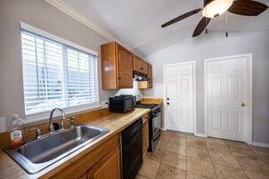 Una cocina con armarios de madera, un lavamanos de acero inoxidable, un microondas, una estufa y un lavavajillas.