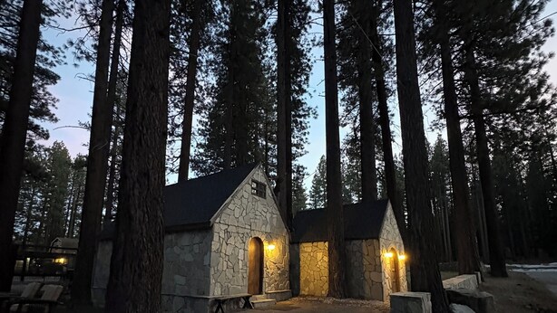 Un edificio de piedra con dos entradas iluminadas, rodeado de altos pinos.