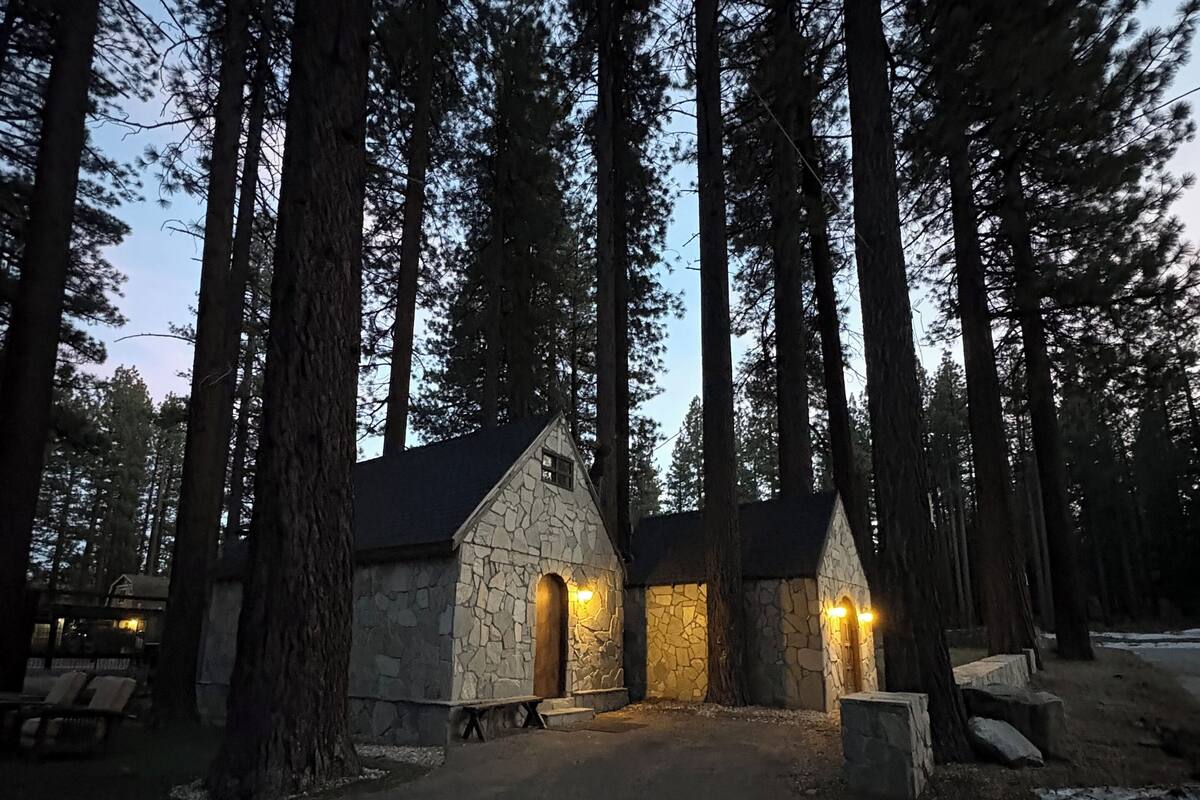 Un edificio de piedra con dos entradas iluminadas, rodeado de altos pinos.