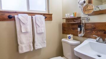 A bathroom with a toilet, sink, and window. There are towels hanging on a rack above the toilet.