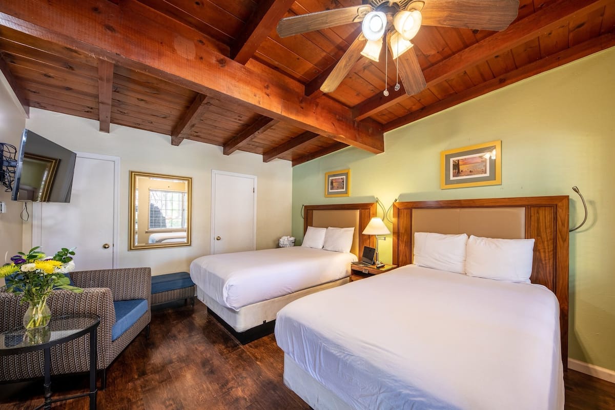 Habitación de hotel con dos camas, techo de madera y una pequeña zona de estar con una mesa y una silla.