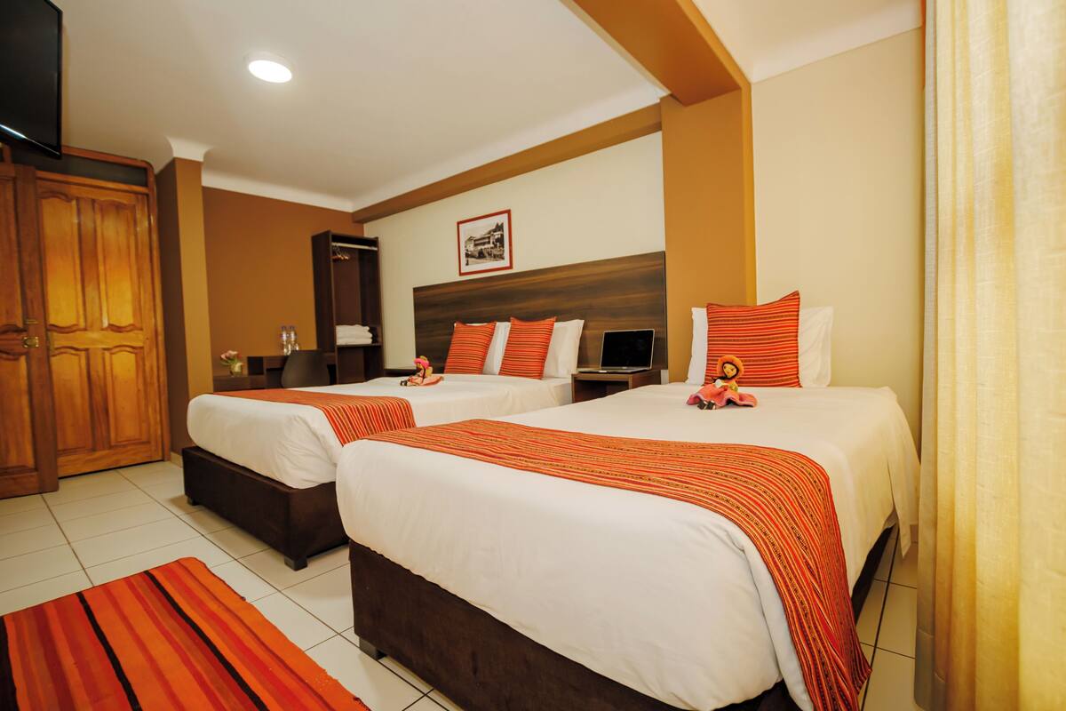 A hotel room with two beds, a wooden wardrobe, a flat-screen TV, and a framed picture on the wall.
