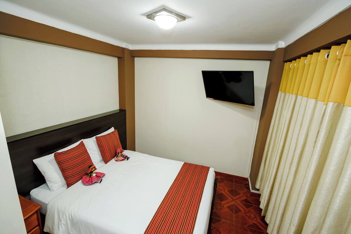 A hotel room with a bed, a TV mounted on the wall, and a curtain.