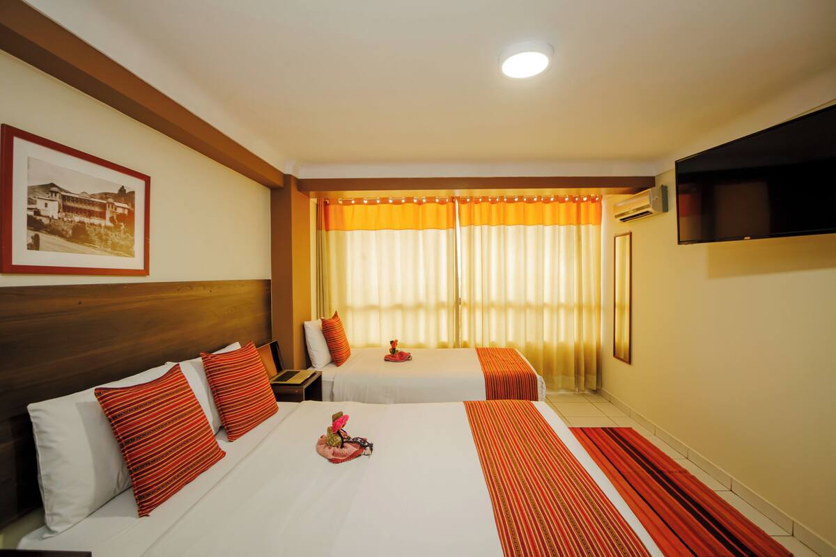 A hotel room with two beds, a flat-screen TV, a framed picture on the wall, and a window with curtains.