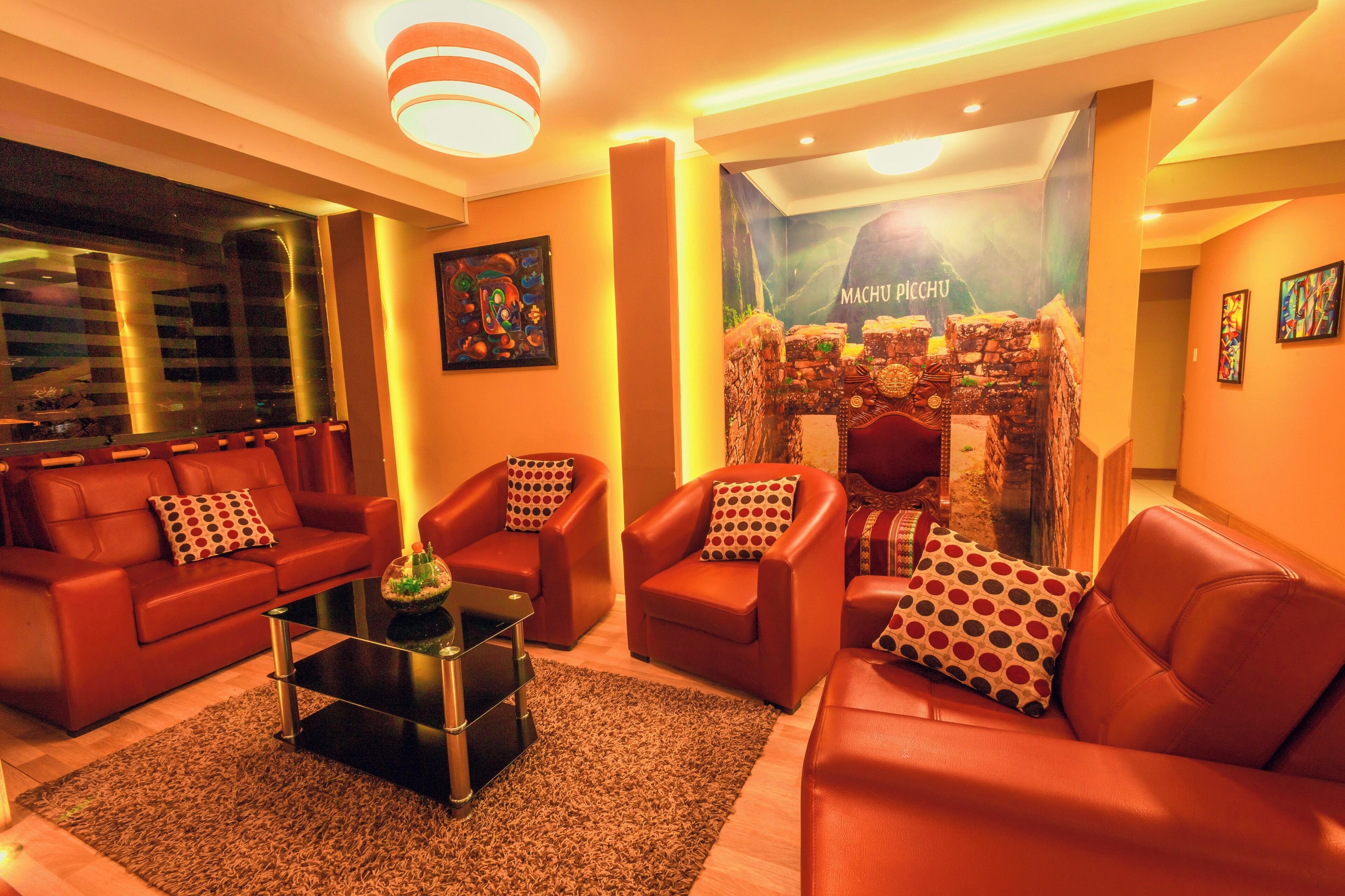 A modern living room with red leather sofas, a glass coffee table, and a large poster of Machu Picchu.