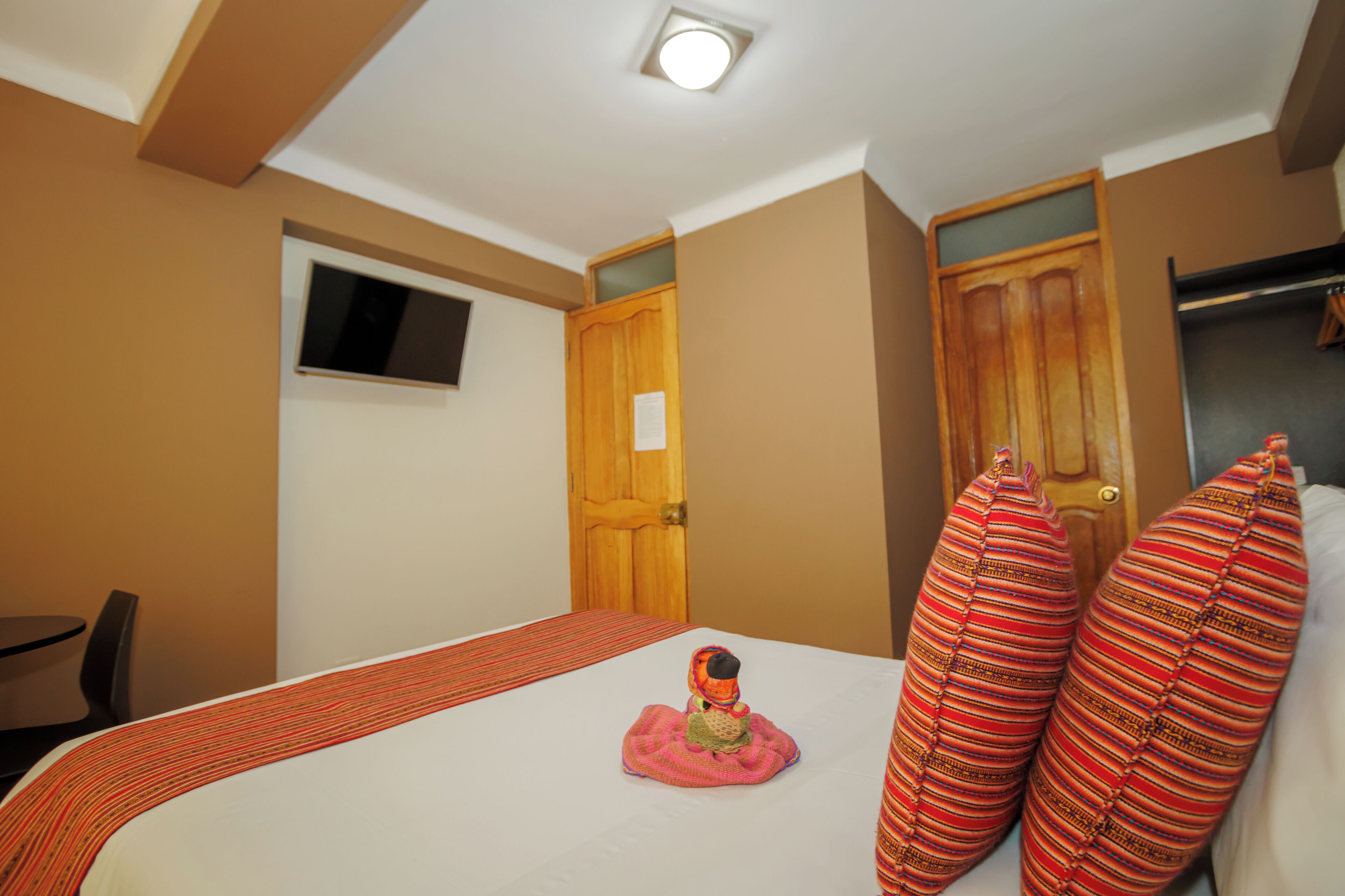 A hotel room with a bed, a wooden door, a small window, and a television on the wall.