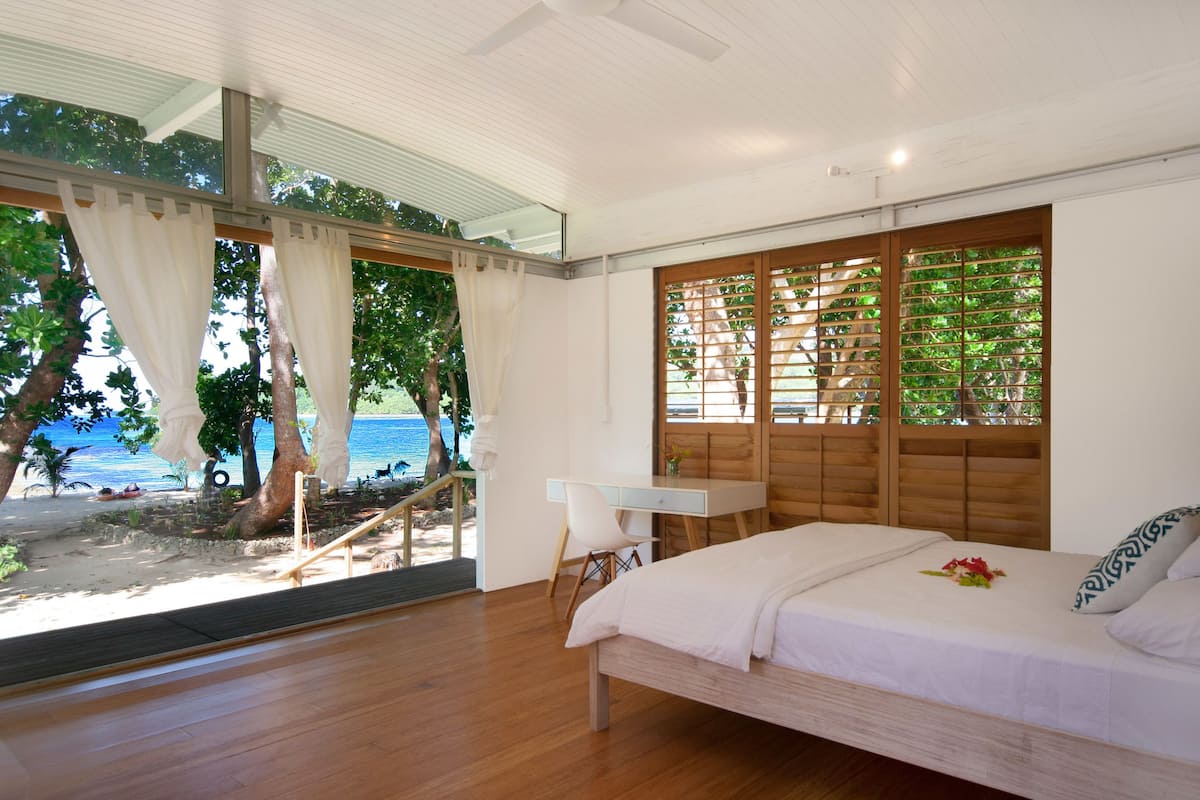 A bedroom with a bed, desk, and a view of the beach and ocean.