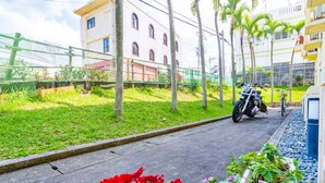 Un camino pavimentado con una motocicleta estacionada al lado, rodeado de follaje y una cerca.