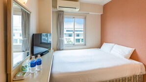 Una habitación de hotel con cama, televisión y ventana con cortinas.