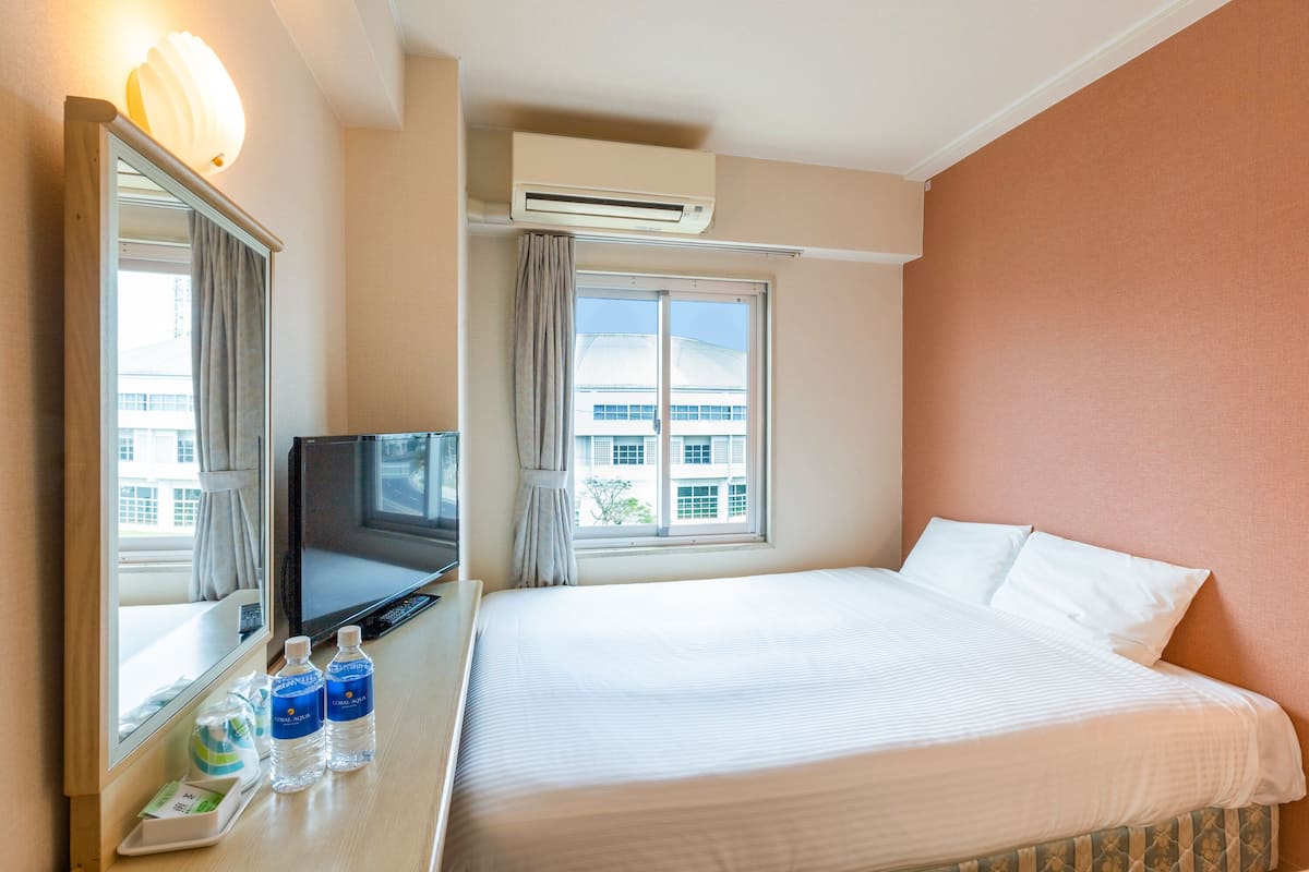 Quarto de hotel com uma cama, televisão e janela com cortinas.
