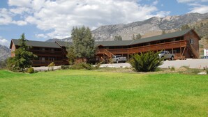 Un amplio refugio de madera con un espacioso jardín delantero y montañas al fondo.