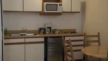 Cocina compacta equipada con microondas, cafetera y lavavajillas. Hay una silla de madera y una mesita redonda.