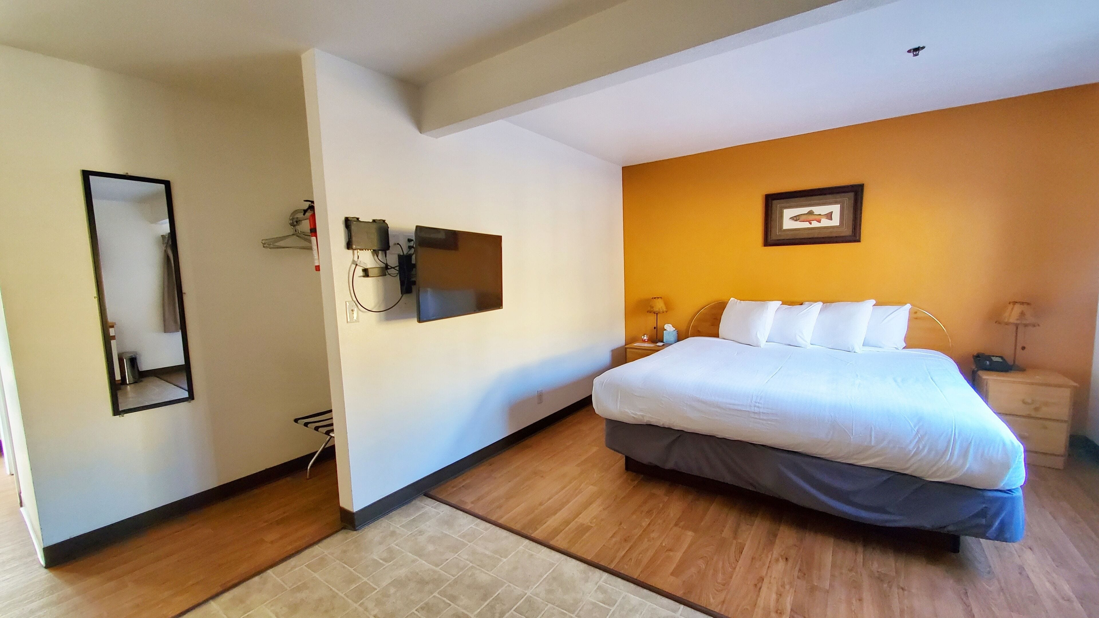 Una habitación de hotel con cama, mesita de noche, lámpara y televisor montado en la pared.