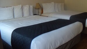Una habitación de hotel con dos camas, cada una con ropa blanca y una colcha acolchada oscura.