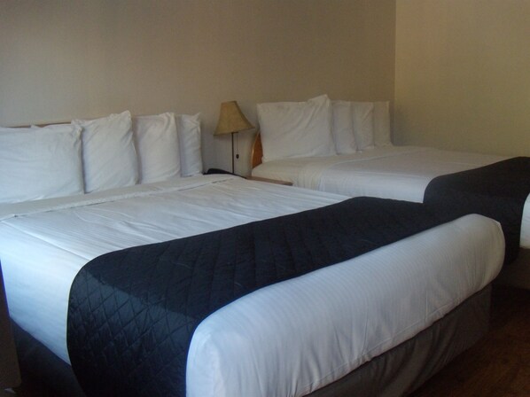 A hotel room with two beds, each with white bedding and a dark quilted bedspread.