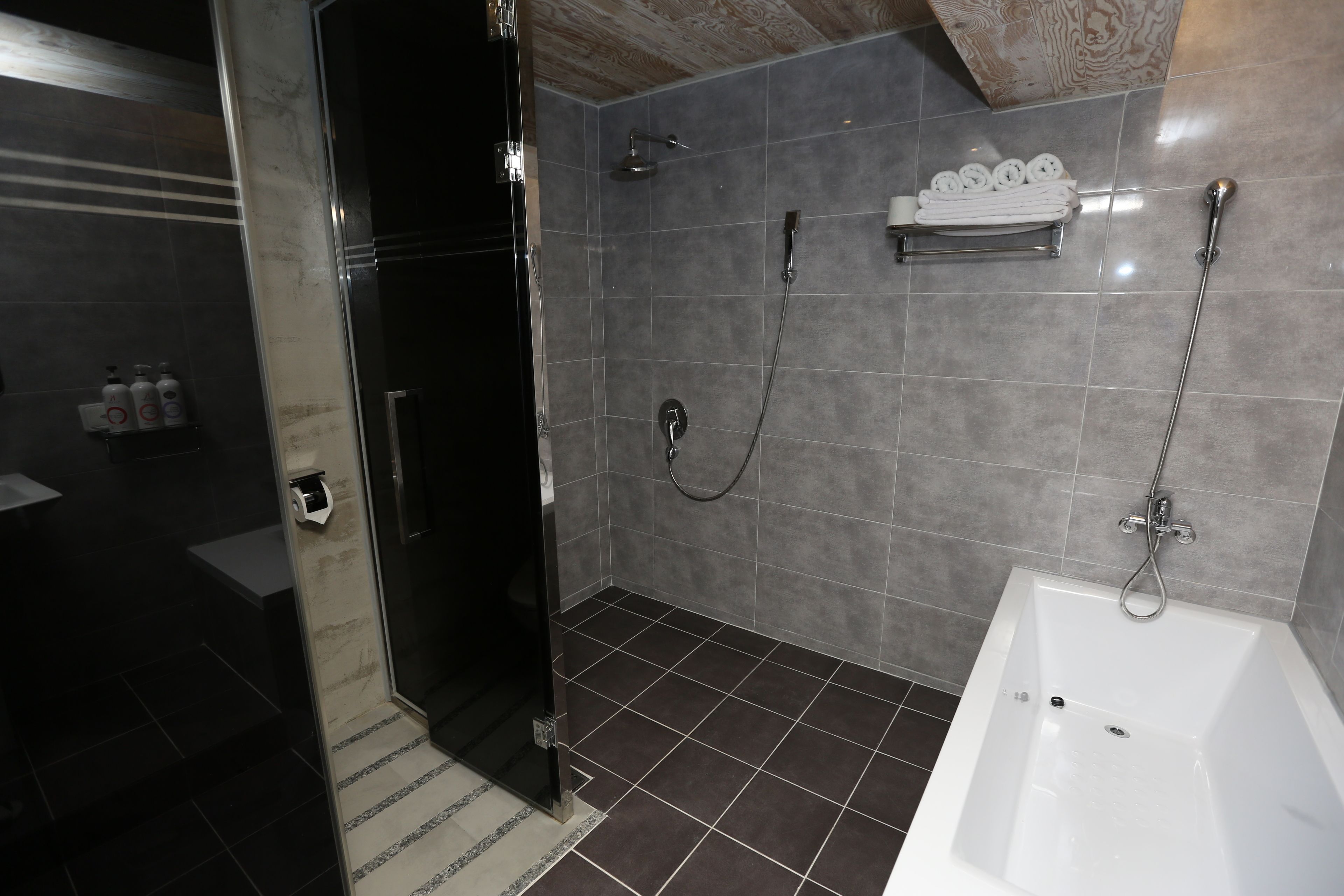 A modern bathroom with a glass shower enclosure, a white bathtub, and a towel rack with neatly folded towels.