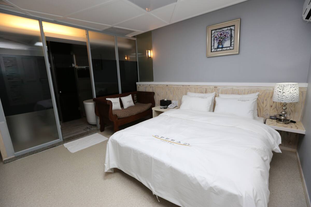 Ein Hotelzimmer mit einem großen Bett, einem Nachttisch aus Holz, einem Schreibtisch, einem Stuhl und einer Schiebetür zum Balkon.