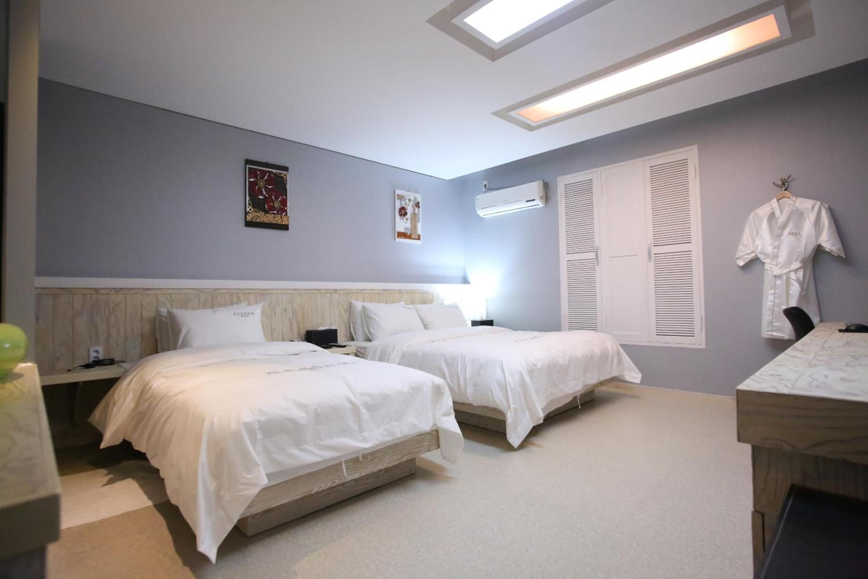 A hotel room with two beds, a desk, and a robe hanging on the wall.