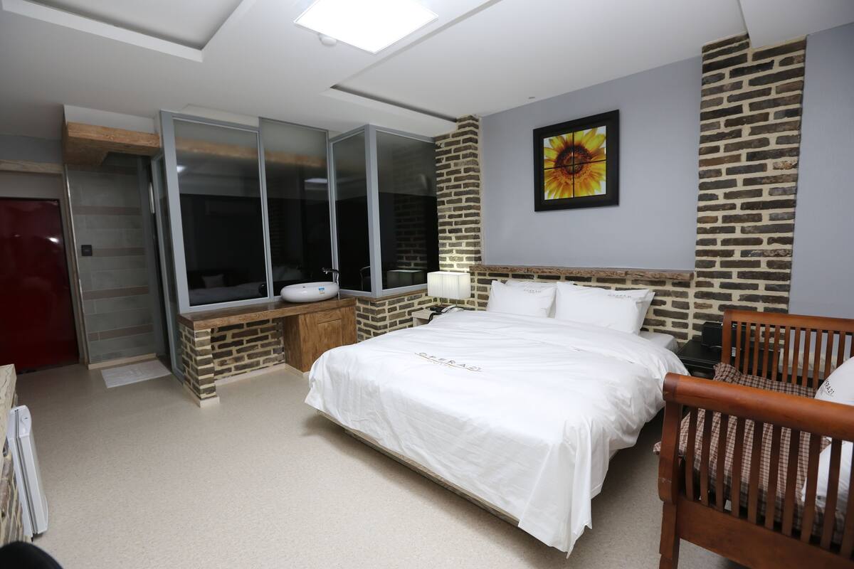Ein Schlafzimmer mit einem großen Bett, einem hölzernen Kopfteil, einem Nachttisch, einem Spiegel, einem Fenster und einer Wand mit Ziegeln.