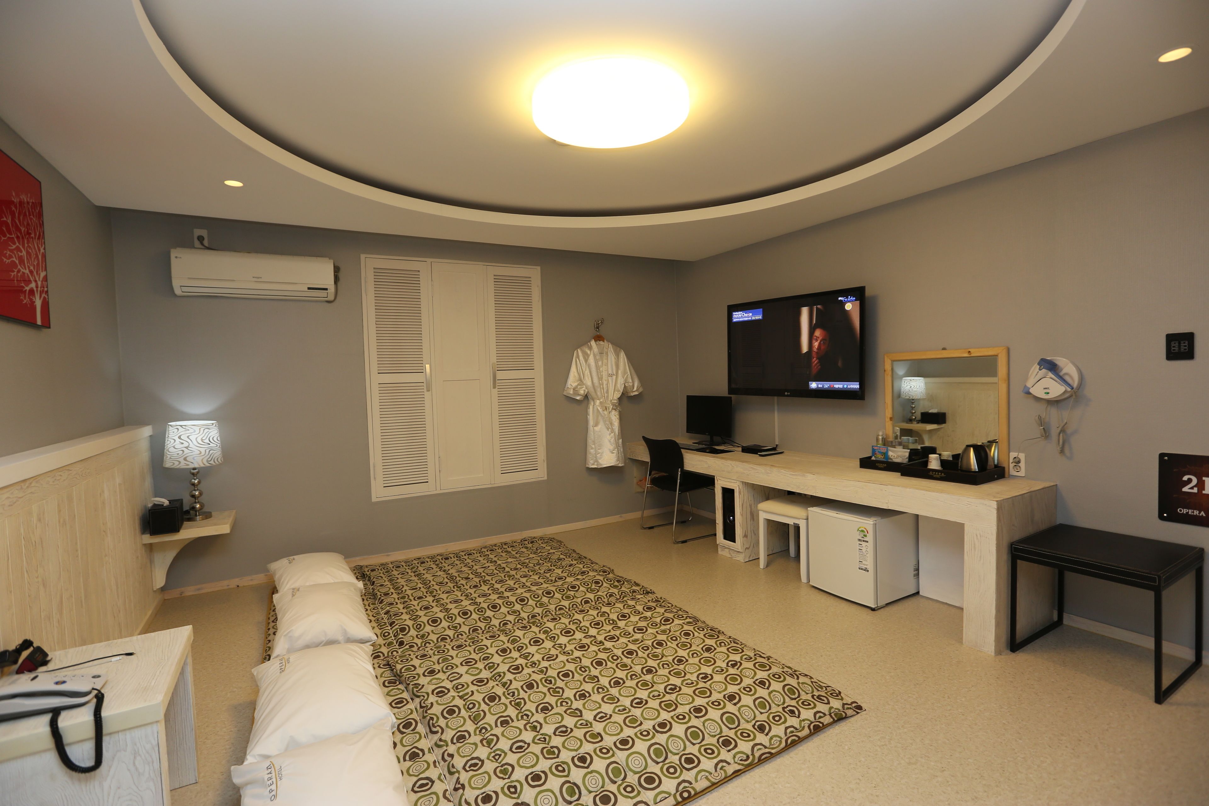 Una habitación de hotel moderna con una cama grande, un escritorio con computadora, un televisor y un refrigerador pequeño.