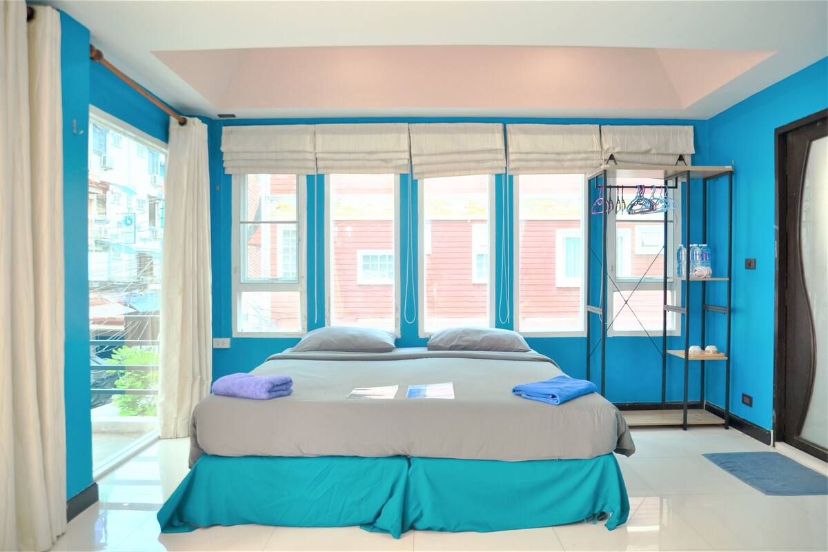 A bedroom with a bed, curtains, a window, and a shelf with items.