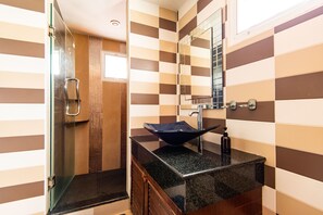 A bathroom with a glass shower enclosure, a black granite sink, and a checkered tile wall. - BGW Phuket - Hostel (Patong)