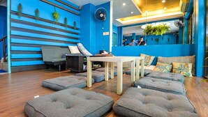 A modern hotel lobby with a blue wall, a reception desk, a seating area with cushioned benches, and a wooden floor. - BGW Phuket - Hostel (Patong)