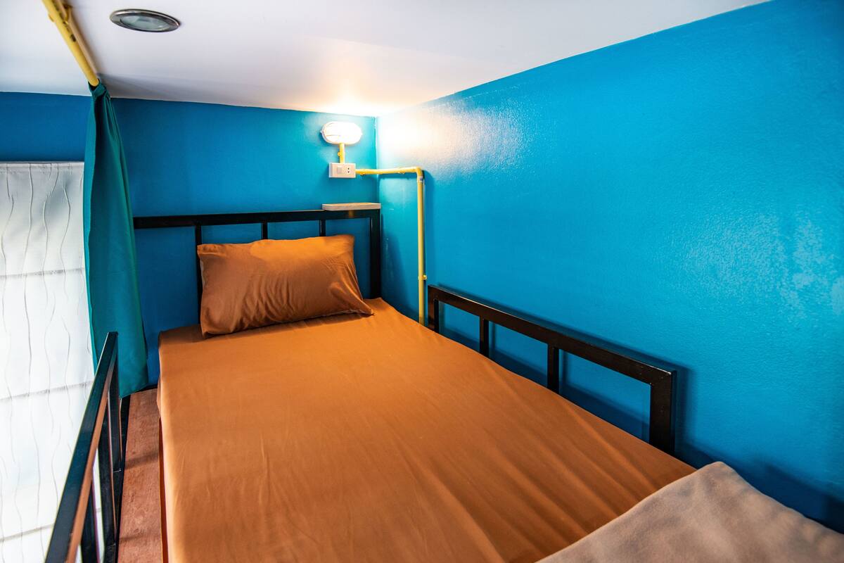 A single bed with a wooden frame in a room with blue walls and a white ceiling.