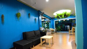 A modern interior with a blue wall, a black sofa, a wooden table, and a ceiling with hanging plants. - BGW Phuket - Hostel (Patong)