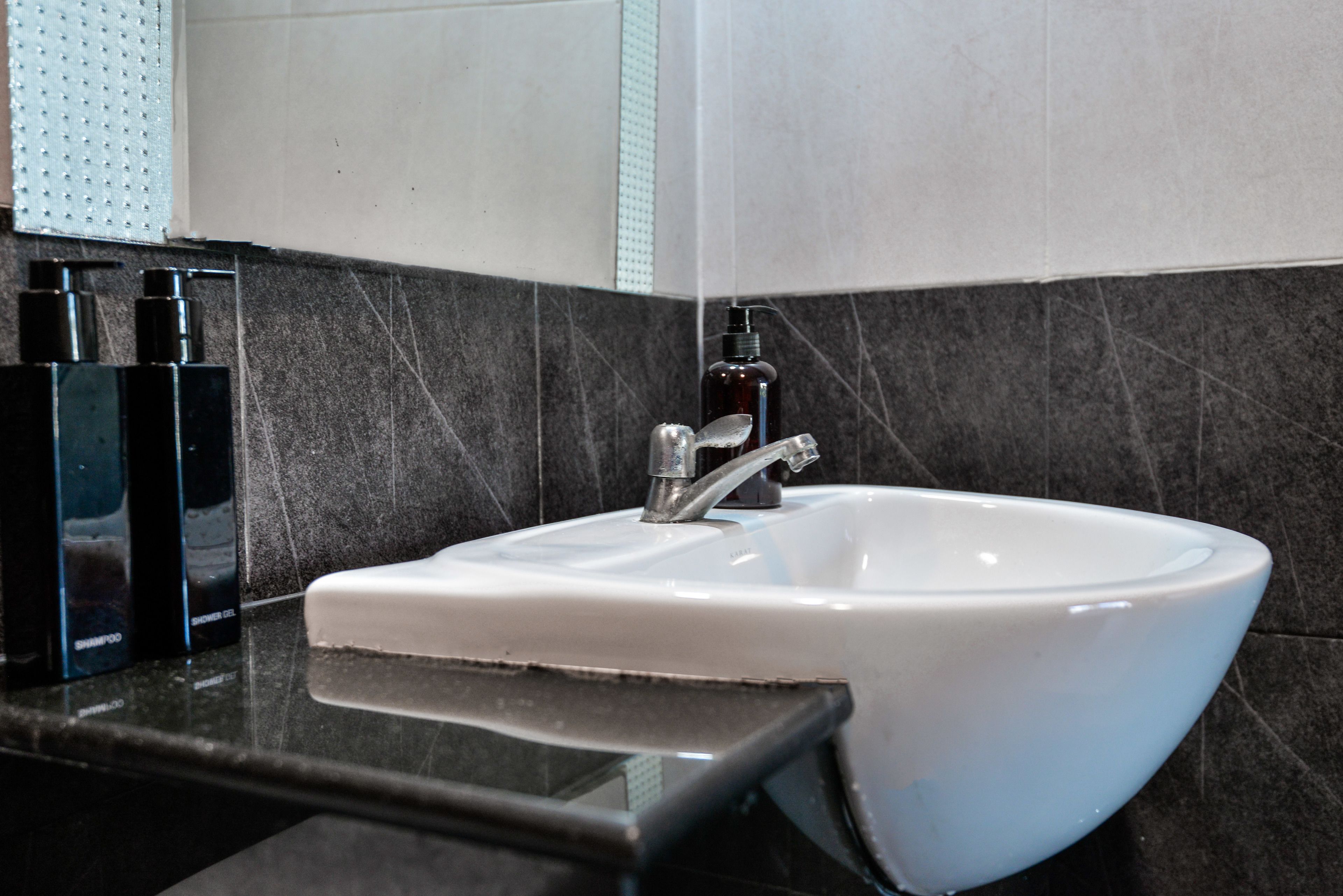 A bathroom with a white sink, dark marble tiles, and a mirror.