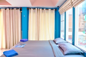 Una habitación de hotel con una cama, almohadas, una toalla azul y una ventana con cortinas.