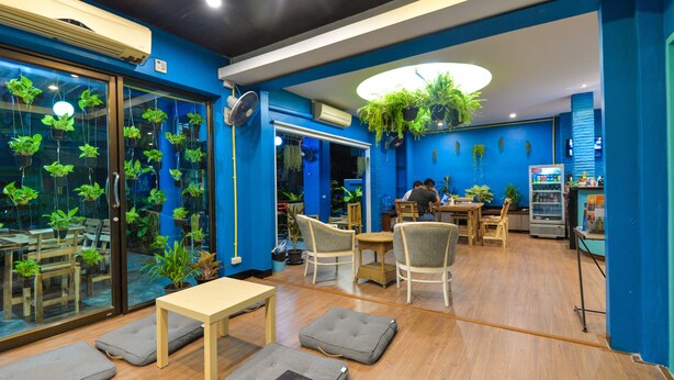 A modern indoor space with blue walls, wooden flooring, and a variety of seating arrangements including tables and chairs. - BGW Phuket - Hostel (Patong)